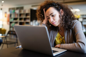 woman with curly hair looks at laptop and thinks about common signs of adhd