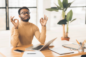 a young man practices the healthy coping mechanism of meditation when he is stressed at work