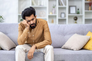 man with head in hands on couch thinking about chronic depression