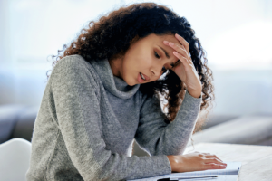 young woman seated at desk with her head in her hands as she struggles with living with generalized anxiety disorder