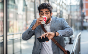 A man with ADHD is walking down the street, and looking at his watch while drinking coffee with caffeine.