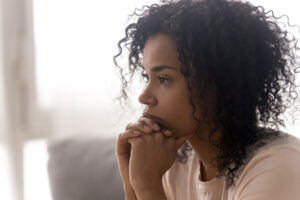 A woman is sitting down with her hands clasped beneath her chin. She looks sad. She's experiencing signs of depression.