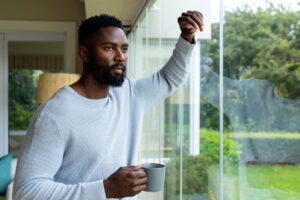 A man with a coffee mug in one hand, leans against the window with his other. Staring outside at something in the distance, he is engaged in a hyperfixation.