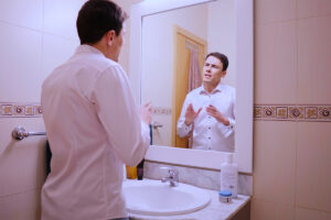 A man rehearses his speech in the bathroom mirror before work. He is experiencing performance anxiety.