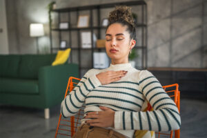 A woman sits with eyes closed. She has one hand on her chest and one on her stomach. She is practicing a technique she learned in ACT.