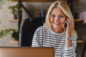 A woman smiles as she uses her laptop and a phone to access virtual therapy at Columbia Mental Health.