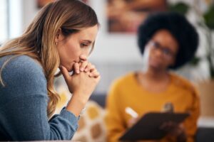 woman with head in hands talks to therapist in yellow sweater